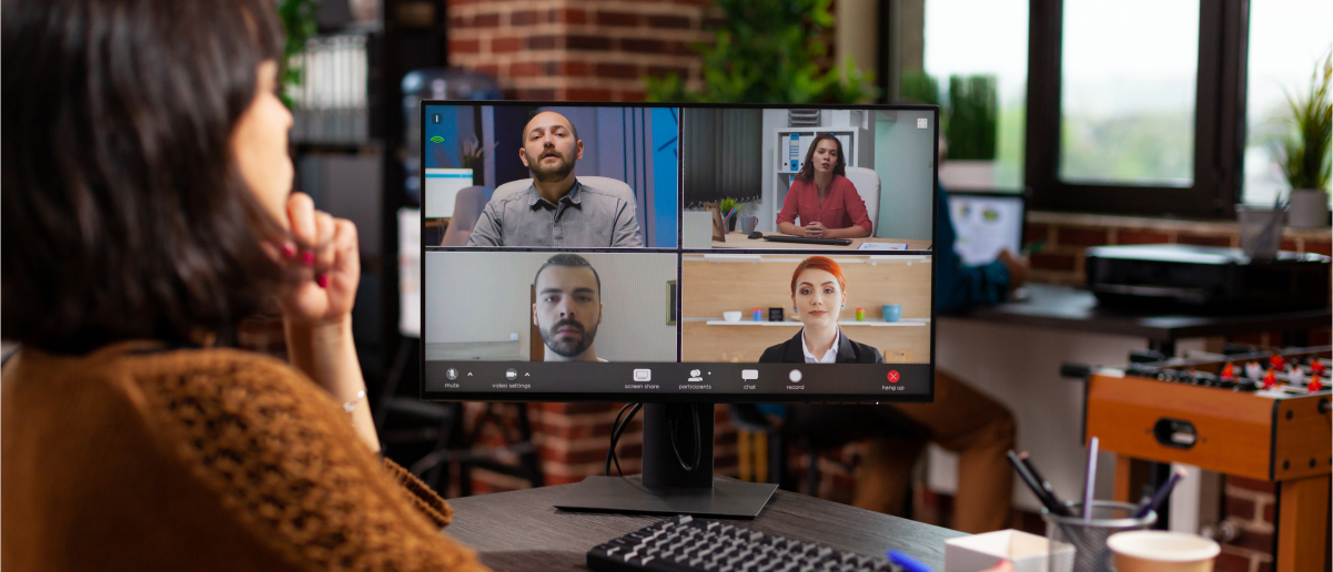 Person in virtual meeting with four colleagues on a computer screen in office.