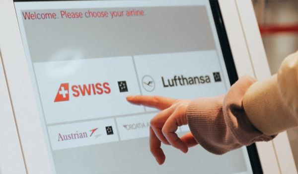 A tourist books flight tickets of SWISS Airlines using an interactive airport digital signage kiosk