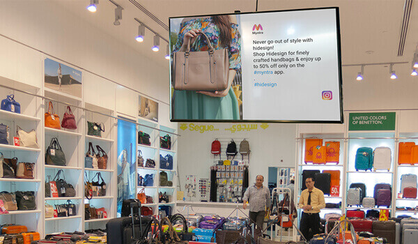 A retail outlet selling bags displays customer testimonials from Instagram on their in-store digital signage screen