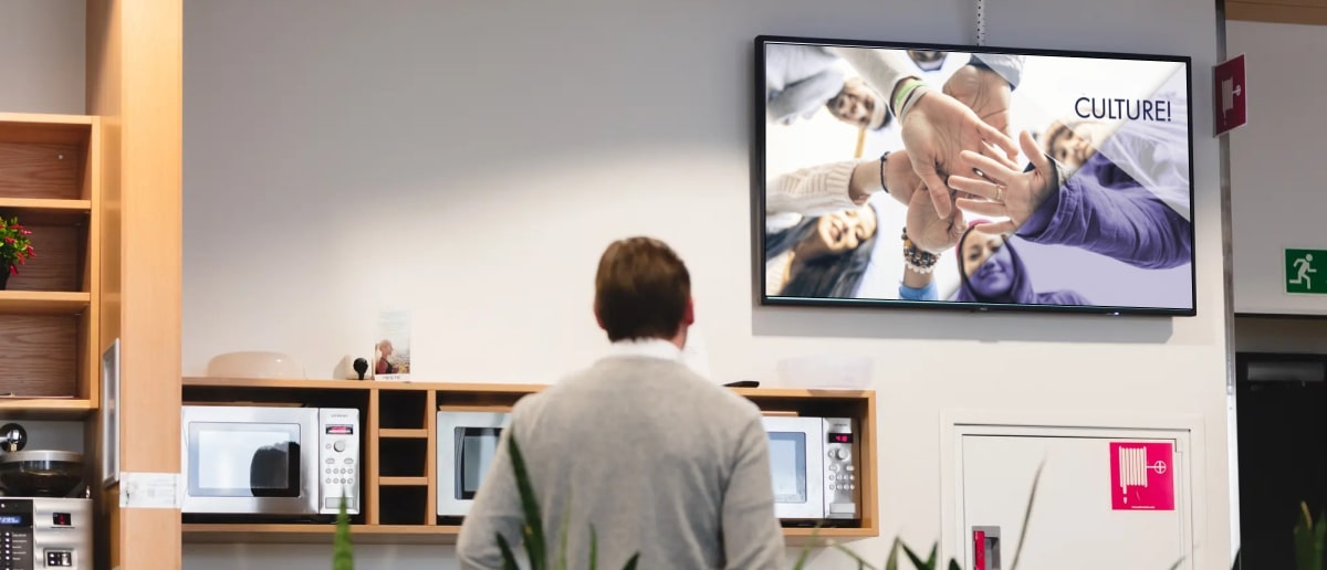 a corporate employee looks at a workplace digital signage showcasing corporate culture video